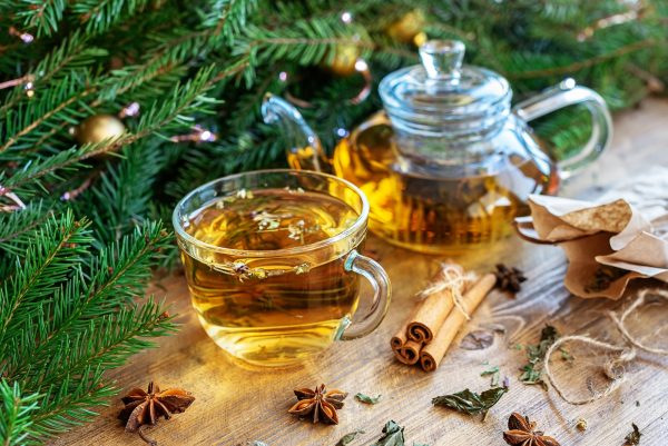 A cup of herbal tea on a wooden table and branches of a Christmas tree with a garland
