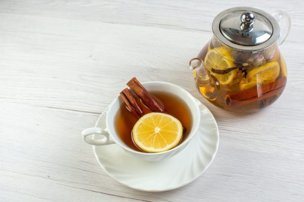 Above view of tea time with mixed herbal tea with lemon in a glass pot on white table